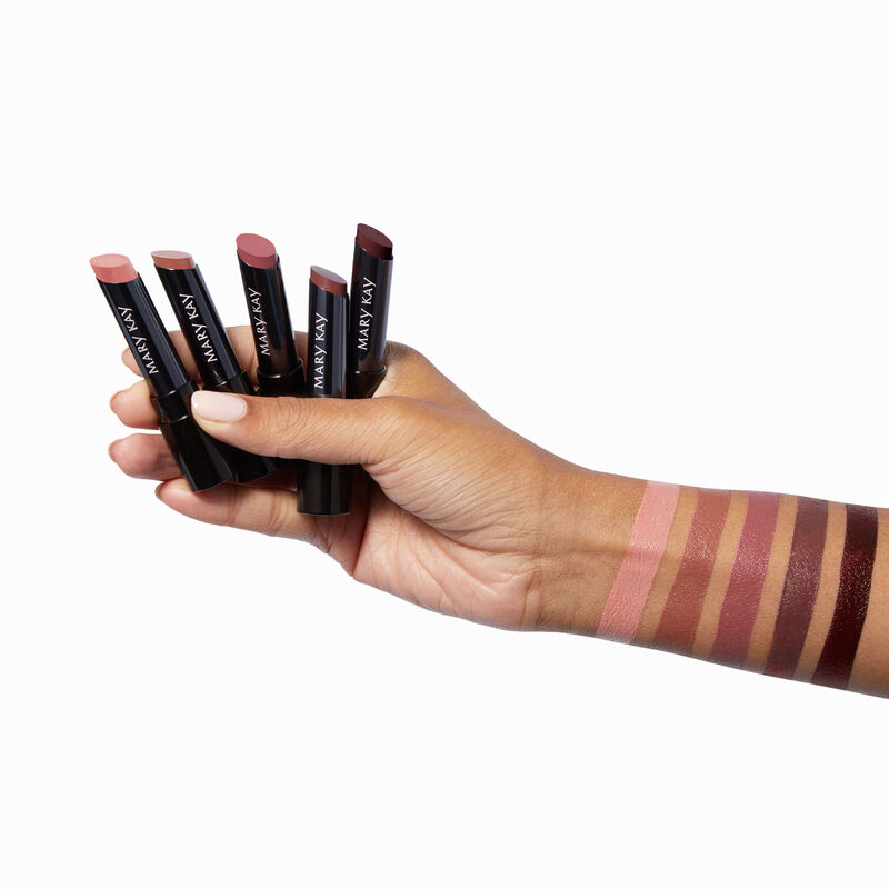 Medium-skinned hand holding five shades of Mary Kay Supreme Hydrating Lipstick with rectangular product swatches down the wrist