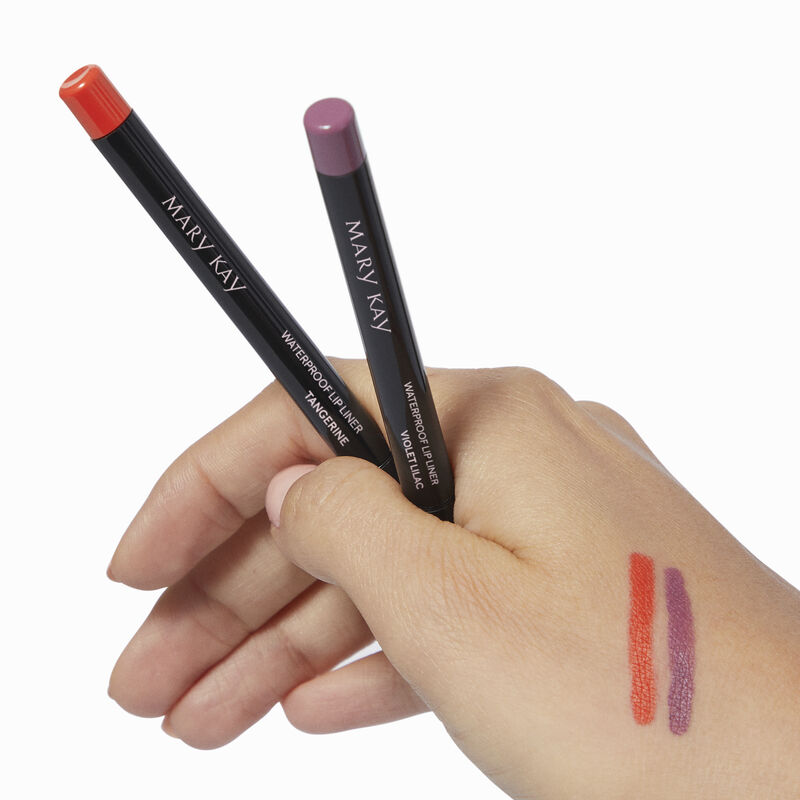 Medium-skinned hand holding special-edition Mary Kay Waterproof Lip Liner pencils in shades Tangerine and Violet Lilac with accompanying product rubs  image number null